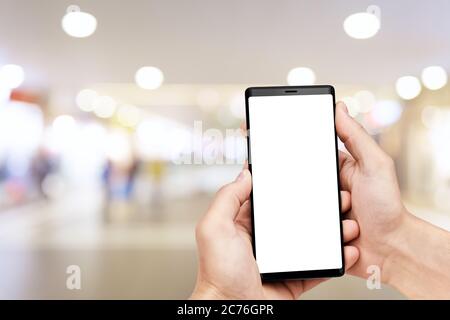 Mann`s Hand hält Handy mit leerem Bildschirm bei verschwommenem Einkaufszentrum Hintergrund. Stockfoto